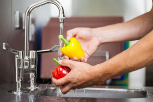 Kitchen porter washing pepper under running tap in professional kitchen