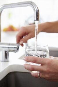 Woman Pouring Glass Of Water From Tap In Kitchen
